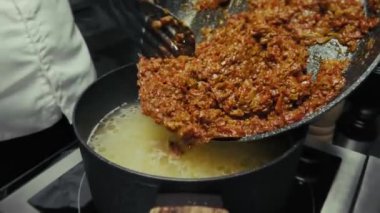 Siyah eldivenli bir aşçı Kharcho çorbası pişirir.