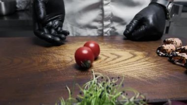 Aşçı ahşap bir tahtada kiraz domatesleri keser.