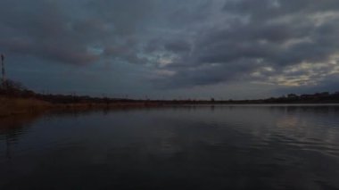 Gün batımında sakin bir gölün nefes kesici panoramik görüntüsü, sakin suya yansıyan ılık renkler.