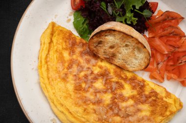 Somonlu omlet, içinde somon dilimleri, taze karışık sebzeler ve kızarmış ekmek tost makineleri ve kızarmış ekmek bulunan yumuşak bir omlet içeren iştah açıcı kahvaltı tabağı.