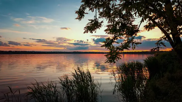 Sakin bir göl üzerinde gün batımı manzarası yumuşak yansımaları ve sakin bir atmosferi var. Ekoloji, çevre ve doğal güzellik konuları için mükemmel..