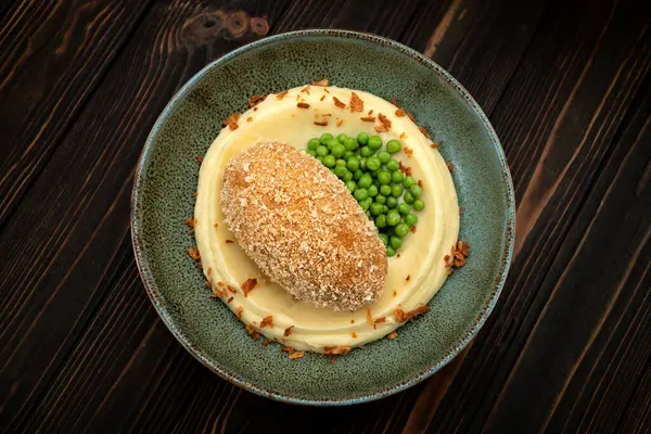 Kremalı patates püresi ve bezelyeyle servis edilen Sulu Kyiv et pirzolası. Stüdyo aydınlatması iştah açıcı sunumu vurgular. Menü tasarımı veya yemek reklamı için mükemmel..