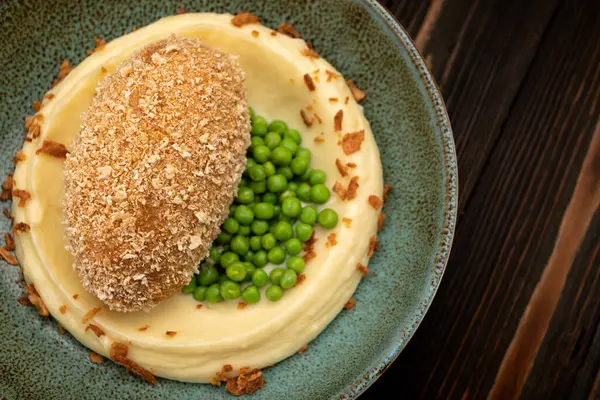 Kremalı patates püresi ve bezelyeyle servis edilen Sulu Kyiv et pirzolası. Stüdyo aydınlatması iştah açıcı sunumu vurgular. Menü tasarımı veya yemek reklamı için mükemmel..