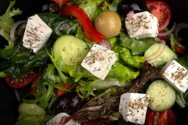 Domatesli, salatalıklı, zeytinli ve feta peynirli taze Yunan salatası, menü tasarımı ve restoran reklamı için koyu bir arka planda..