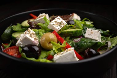 Domatesli, salatalıklı, zeytinli ve feta peynirli taze Yunan salatası, menü tasarımı ve restoran reklamı için koyu bir arka planda..