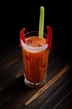 Koyu, ahşap bir yüzeyde bir bardakta servis edilen klasik bir Bloody Mary kokteyli..