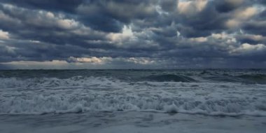 Güçlü fırtınalı deniz dalgaları dramatik bir gökyüzünün altında köpükle.