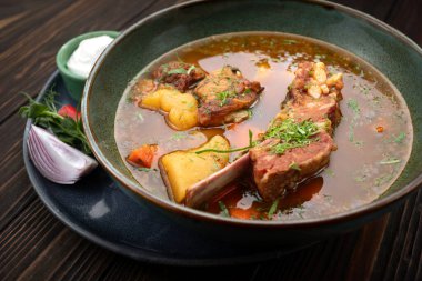 Geleneksel kuzu shurpa çorbası kırsal ahşap masada sos ile servis edilir.