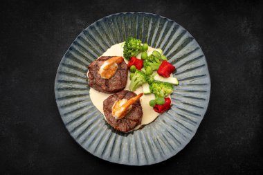 Lezzetli ızgara et madalyonları karides, sebze ve sosla servis edilir..