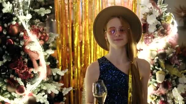 圣诞晚会上的快乐和欢乐的情绪 除夕之夜 戴着帽子和粉色眼镜的女孩拿着一杯闪烁着火花的葡萄酒 背景是装饰过的圣诞树 高质量的4K镜头 — 图库视频影像
