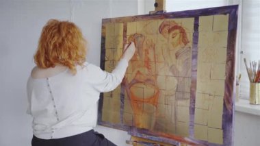 Beyaz kadın ressam, atölyenin iç kısımlarındaki tuvalde boya fırçasıyla resim çiziyor. Sanat eseri, yaratıcı resim. Sanat stüdyosundaki tuvale resim yapan genç bir kadın sanatçı. 4k video kaydı