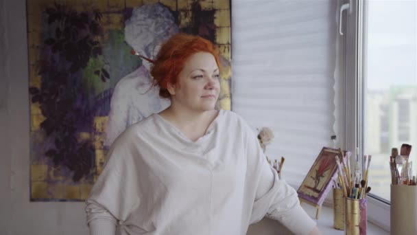 窓枠に筆で考える赤毛のアーティストの女性の肖像画 キャンバスにアートワークを背景にポーズをとる画家 高品質4K映像 — ストック動画