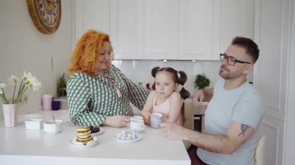 快乐的高加索父母和可爱的小女孩早上一起在家里厨房的饭桌上吃早餐 桌上放着煎饼的茶 家庭周末概念4K视频镜头 — 图库视频影像