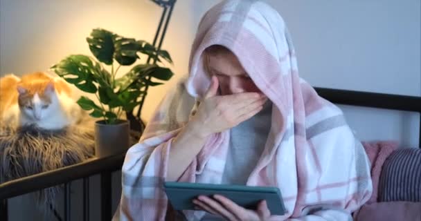 自宅やオンライン学習からの仕事 彼の近くの毛布と白いタビー猫で覆われたベッドの中でタブレットを使用している間 若い男をくしゃみひげ 病気や病気の概念を感じる 4Kビデオ映像 — ストック動画