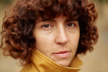 Kameraya bakan güzel, esmer bir kız. Kızıl saçlı kıvırcık beyaz kadın sonbahar açık hava portresi. Sonbahar sezonu. Yüksek kalite fotoğraf