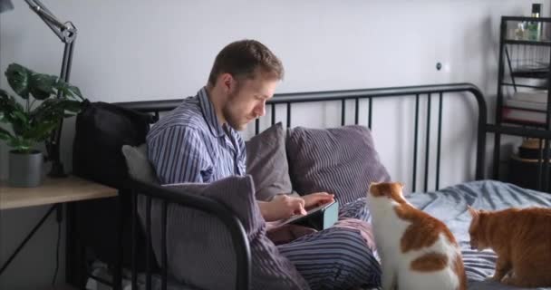 Pemuda Berjenggot Kaukasia Menggunakan Tablet Duduk Tempat Tidur Mengenakan Piyama — Stok Video