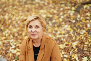 Sonbahar sezonu ya da emeklilik: Sonbahar parkında oturan beyaz bir kadının yakın plan portresi. Gülümseyen olgun insanlar doğanın tadını çıkarıyorlar. Yüksek kalite fotoğraf
