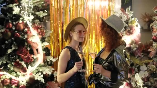 背景にライトと話す白人の陽気な女性の友人 クリスマス2023パーティー中の幸せと楽しい感情 帽子の女の子は大晦日の間にスパークリングワインのグラスを持っています 4Kビデオ — ストック動画