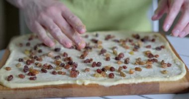 Ev konseptinde kabuk hazırlama. Tanınmayan kişi yoğurulmuş hamura tereyağı sürülmüş kuru üzüm serper. Erkek tereyağlı hamurun üzerine kuru üzüm döker. Yüksek kalite 4k video kaydı