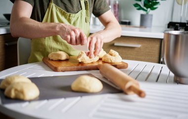 Yeşil önlüklü, hamuru parçalara ayıran tanınmamış erkek aşçı. Kesme tahtasına spatula kullanarak hamur kesmek. Ev yapımı mutfak konsepti, ev yapımı pişirme. Yüksek kaliteli resim