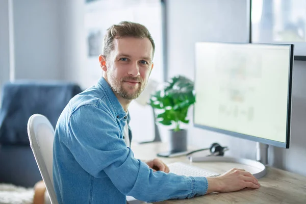 年轻英俊的It支持着穿着牛仔衬衫的男人 有吸引力的大胡子男性自由职业软件工程师坐在办公室里 很少用电脑工作 高质量的图像 免版税图库照片