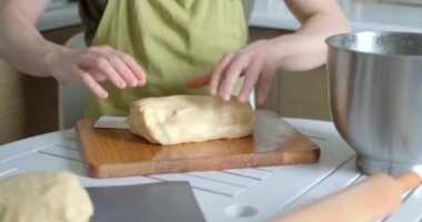 Yeşil önlüklü, hamuru parçalara ayıran tanınmamış erkek aşçı. Kesme tahtasına spatula kullanarak hamur kesmek. Ev yapımı mutfak konsepti, ev yapımı pişirme. Yüksek kalite 4k video kaydı