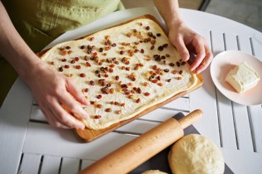 Ev kavramında paskalya pastası ya da kabuk hazırlama. Baker tereyağlı hamurun üzerine kuru üzüm döker. Tanınmayan bir erkek, yoğurulmuş hamura tereyağı sürülmüş kuru üzüm serper.