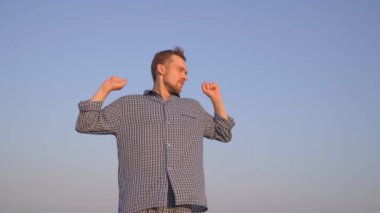 Sabah esnemesi: Çekici sakallı beyaz adam dışarıda dikiliyor uyku elbisesi giyiyor ve yan tarafa bakıyor. Arkadaki açık mavi gökyüzü. Rahatlatıcı bir sabah ya da sakin bir konsept. Yüksek kalite 4k görüntü