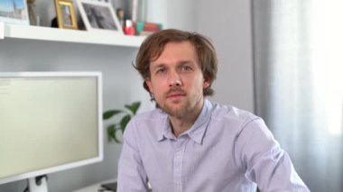 Young handsome IT support man in shirt . Attractive bearded caucasian male freelance software engineer sitting at working place in office with computer on background. High quality 4k video footage