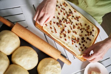 Easter pastry or cruffin preparation at home concept. Baker pours raisins on a buttered rolled dough. Rolling kneaded dough smeared with butter. High quality image