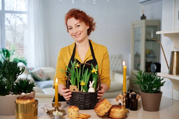 woman smiling with daffodils basket and easter cakes, burning candles at home. Preparation for easter High quality photo