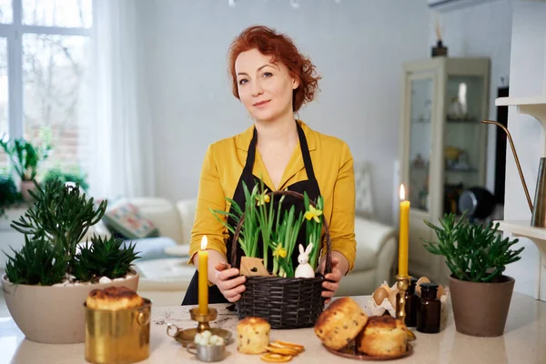 woman smiling with daffodils basket and easter cakes, burning candles at home. Preparation for easter High quality photo