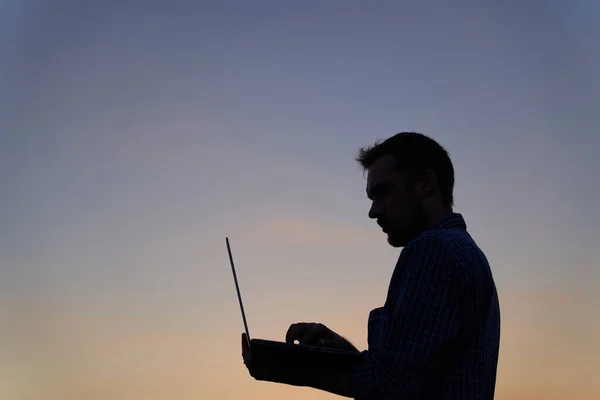 IT male engineer or freelancer in silhouette working outdoor using laptop. Sunset time. Adorable dusk at background. Hardly working evening. High quality image
