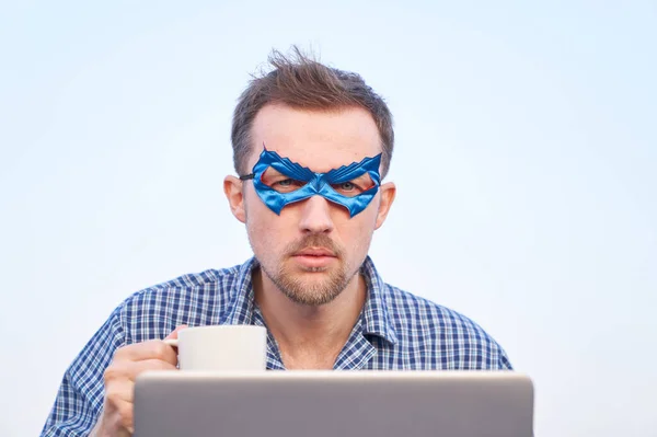Itサポートスーパーヒーロー男ホットティーやコーヒーのノートパソコン保持カップを使用しています ナイトウェアのシャツを着た陽気な男とノートパソコンを屋外で使用して青い顔のマスク 高画質 — ストック写真