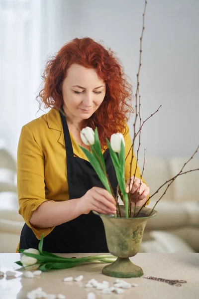 Making tulip bouquet: female caucasian redhead florist portrait in yellow dress and black apron is working. Florist, plants care and gardening concept. High quality image