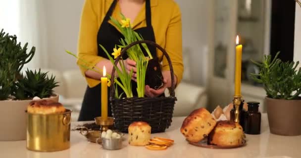 复活节准备的概念 花匠女人把水仙花插在篮子里 烛台上 一个叫做Kulich的复活节糕点和一个桌子上的鸡蛋作为复活节装饰 优质4K影片 — 图库视频影像
