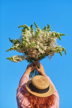 Pembe tişörtlü kadın elinde mavi gökyüzünün arka planında bir buket beyaz çiçek tutuyor, yaz, bahar konsepti. Yüksek kalite fotoğraf