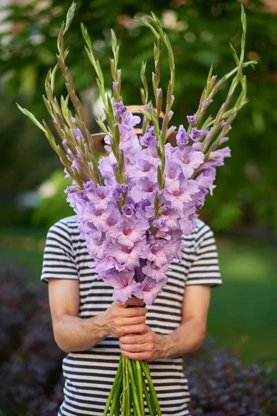 man smiling holding a bouquet of purple gladioluses flowers no face seen on the background of green garden. summer concept High quality photo