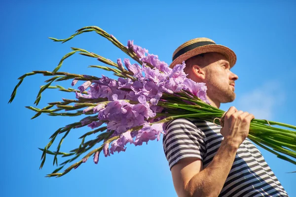 Чоловік Посміхається Тримаючи Букет Фіолетових Квітів Гладіолусів Виглядають Фоні Зеленого — стокове фото