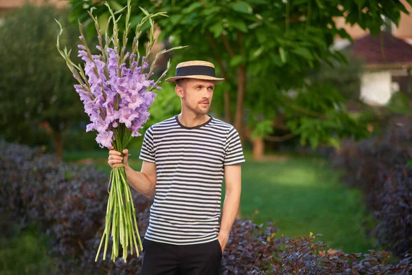 男人笑着拿着一束紫色的角斗士花 在绿色花园的背景上看着相机 夏天的概念高质量的照片 — 图库照片