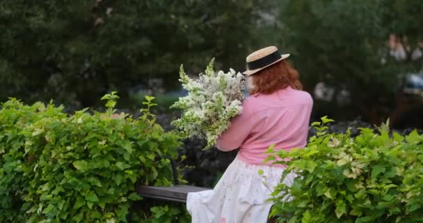 穿着粉红衬衫的女人拿着一束白花 背景是绿色的花园 春天的概念 4K镜头 — 图库视频影像