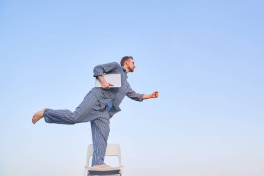 Gözlüklü neşeli sakallı beyaz adam dışarıda bir sandalyede duruyor ve elinde dizüstü bilgisayarla ileriye bakıyor. Sabah iş zamanı konsepti. Yüksek kaliteli resim