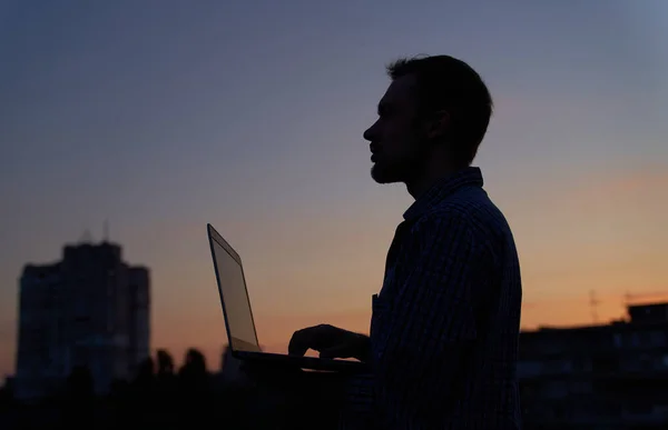 Itサポートエンジニアのフリーランスの男性や開発者は 都会的な背景を持つ日没のシルエットでラップトップを使用して屋外で働いています 背景に愛らしい夕暮れ 高画質 — ストック写真