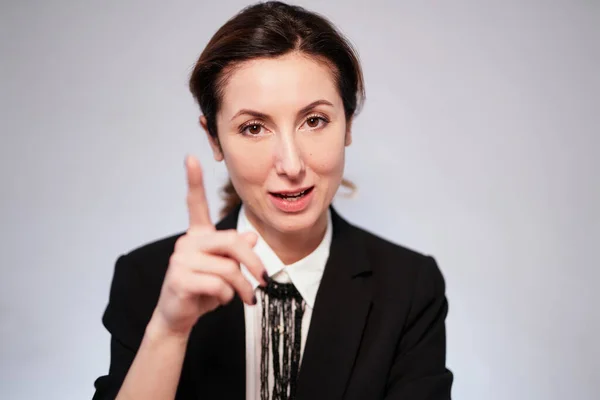 Cheerful manager woman in dark suit pointing with finger and looking into camera. Smiling business lady in black jacket posing on isolated background. High quality photo
