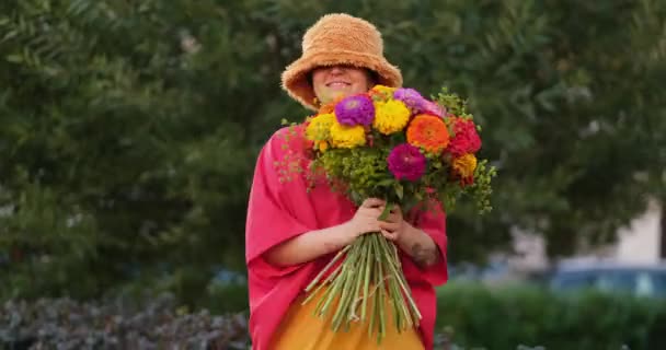 ダンスや面白い動きの概念を作る 緑の庭の背景に赤 オレンジ 黄色の菊の花の花束を保持する愛らしい白人女性 高品質4Kビデオ映像 — ストック動画
