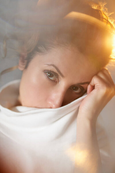 Warm light close-up portrait concept. Emotional looking young woman looking at camera, thinking and dreaming of something. High quality vertical photo