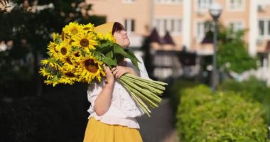 Açık havada sarı etekli, gülümseyen bir kadının ellerinde kocaman bir buket taze ayçiçeği. Vatansever hediye, sevgi ve minnettarlık. Anneler Günü. Ukrayna 'ya destek. Bağımsızlık Günü. Yüksek kalite 4k video