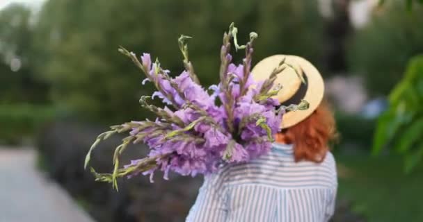 Mujer Pelirroja Camisa Azul Sombrero Caminando Sosteniendo Ramo Gladiolos Púrpura — Vídeo de stock