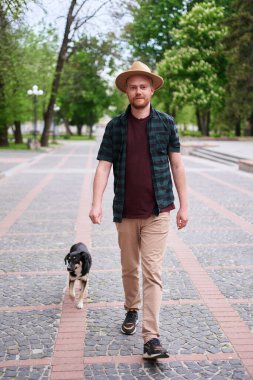 Şapkalı genç adam kurtarılmış köpeğini gezdirip dışarıdaki kameraya bakıyor. Barınaktaki köpek yeni bir ev buldu. Yüksek kaliteli fotoğraf.