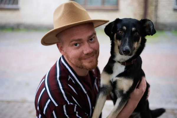 Happy young man in hat hugging his rescued dog looking at the camera outdoors. Dog from the shelter found new home High quality photo